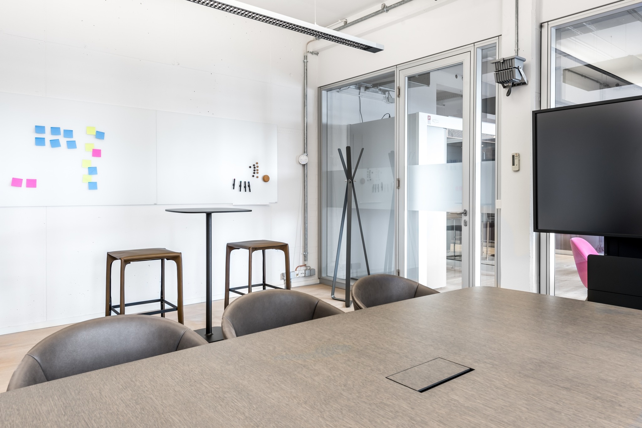 Moderner Konferenzraum mit Besprechungstisch, Stühlen, Whiteboard und einer Garderobe.