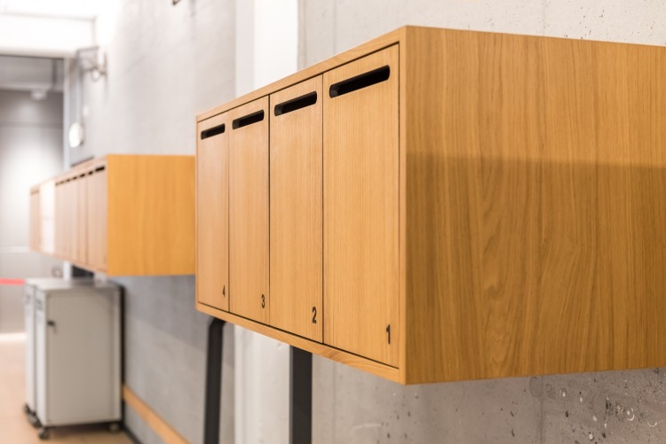 Locker aus Holz mit Nummerierung und Briefschlitz an einer Betonwand aufgehängt
