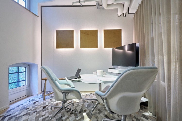 Besprechungsraum mit Tisch, Monitor und 2 Sesseln. An der Wand akustische Leuchten.