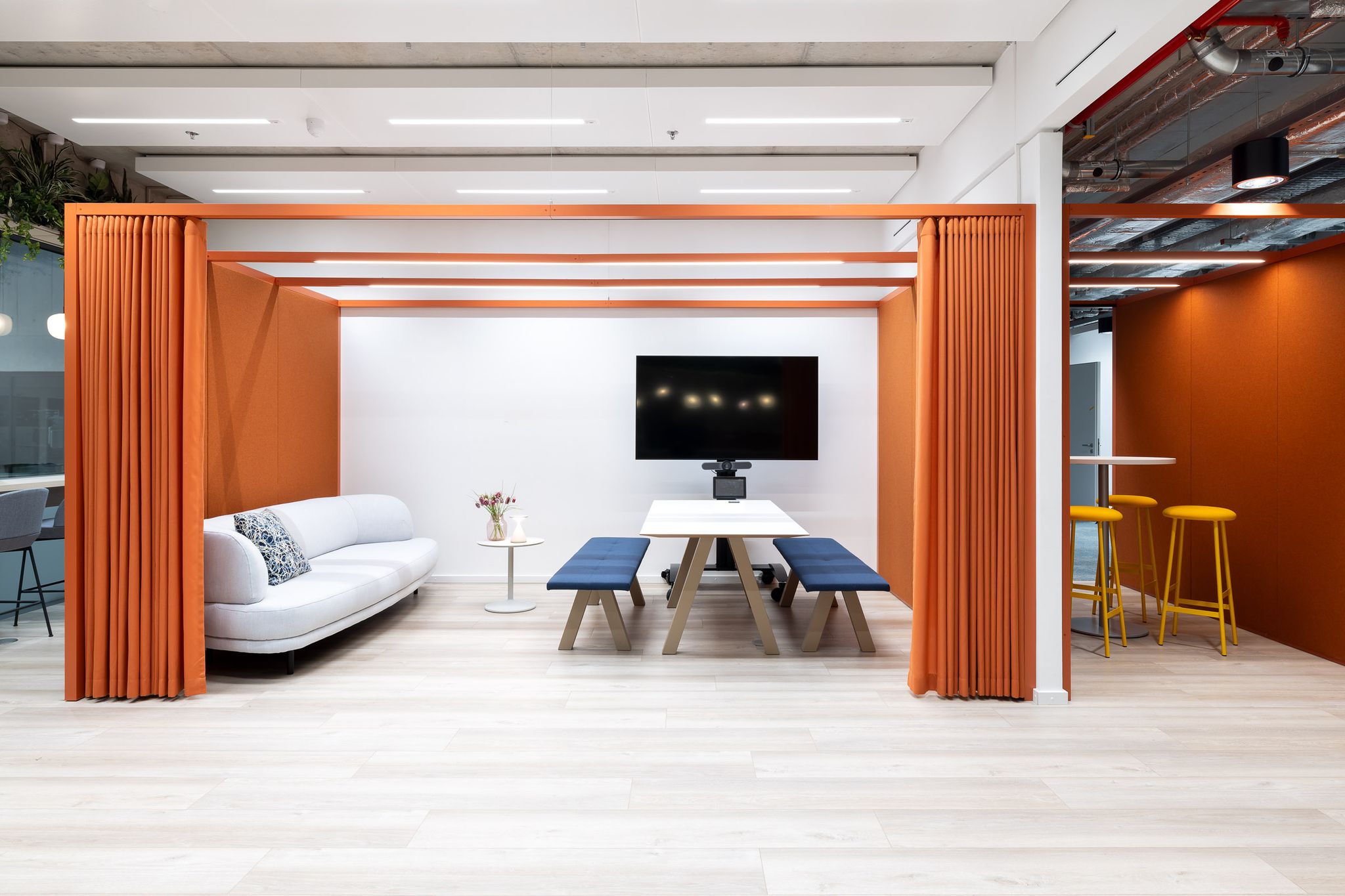 Sofa links, rechts daneben Sitzbank mit Tisch und Bildschirm dahinter an der Wand