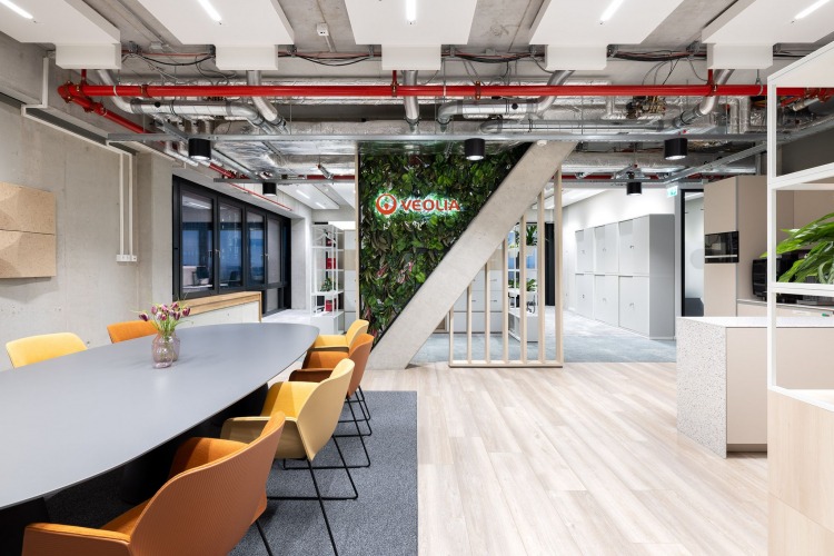 Offener Küchenbereich; Esstisch mit gelben Stühlen und eine Pflanzwand mit rotem Veolia Schriftzug