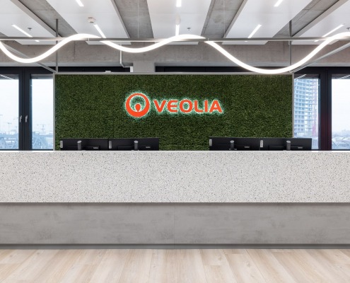 Empfangstheke, dahinter ein Veolia Schriftzug in rot auf grünem Mooshintegrund